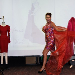 Lorelei Shellist, Image Consultant, on stage wearing a colorful dress and flowing scarf, mannequin with red dress
